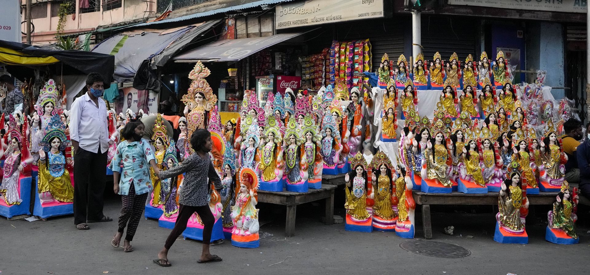 Un niño y una niña caminan junto a los ídolos de Saraswati, la diosa hindú del aprendizaje,en un puesto de venta al borde de la carretera antes de su culto programado para el sábado, en Calcuta, India, el jueves 3 de febrero de 2022.
