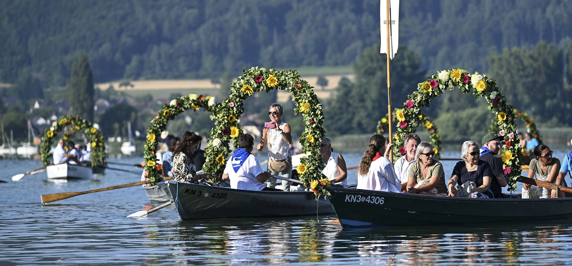Barcos decorados con coronas de flores navegan por el lago Constanza hasta la orilla de Radolfzell durante la procesión acuática de Moos en Radolfzell am Bodensee, Alemania, el lunes 18 de julio de 2022.