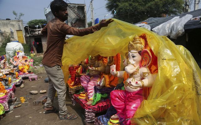 Un trabajador cubre un ídolo del dios hindú con cabeza de elefante Ganesha preparado para la venta para el próximo festival Ganesh Chaturthi