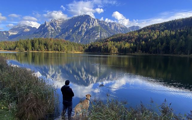 Un hombre y su perro contemplan las montañas de los Alpes en un lago cerca de Mittenwald