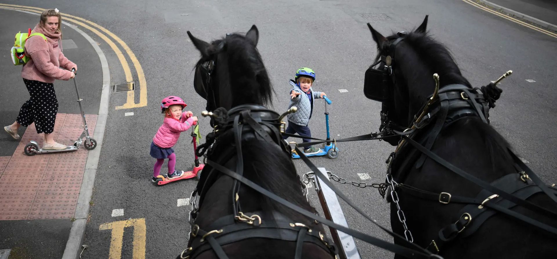 Una mama con sus niños cruzan la calle frente a un carro tirado por caballos que entrega cervezas, incluida una hecha por Windsor & Eton Brewery, para conmemorar los 70 años de la Reina en el trono. Fotografía: Daniel Leal/AFP/Getty Images