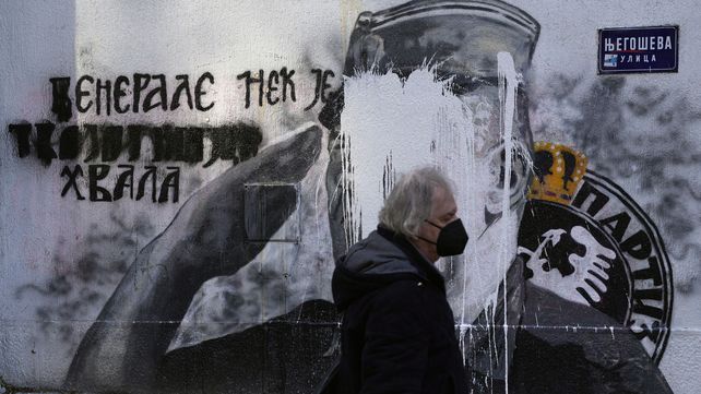 Un hombre camina junto a un mural del exjefe militar serbio de Bosnia, Ratko Mladic, destrozado con pintura blanca en Belgrado, Serbia, el miércoles 10 de noviembre de 2021. La policía se desplegó en el lugar de la gran pintura en Belgrado de los serbios de Bosnia convictos en tiempo de guerra, comandante Ratko Mladic, que los activistas de derechos querían eliminar. 