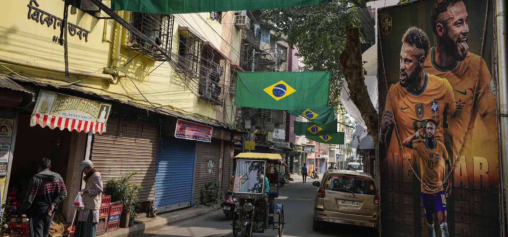 La gente camina por una calle decorada con Neymar de Brasil junto con banderas colocadas por fanáticos para conmemorar la Copa Mundial de fútbol en curso en Kolkata, India, el jueves 8 de diciembre de 2022. (Foto AP / Bikas Das)