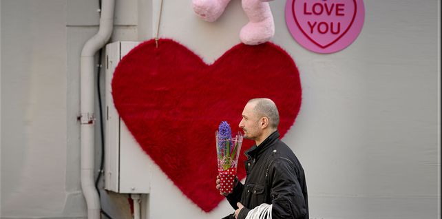 Un hombre que sostiene una maceta con una flor camina junto a una figura en forma de corazón en Bucarest