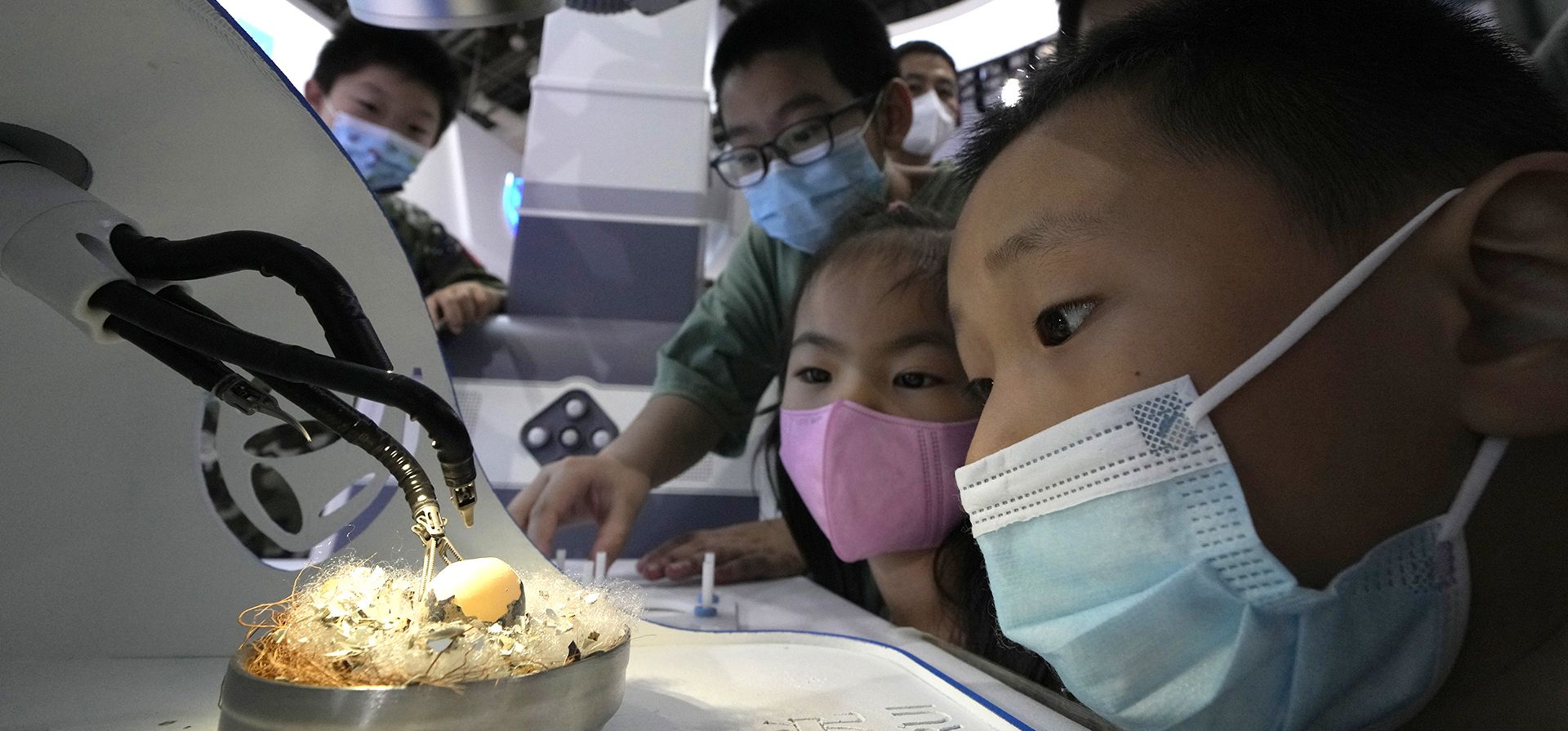 Niños con mascarillas observan cómo un robot quirúrgico demuestra su destreza quitando la cáscara de un huevo durante la Conferencia Mundial de Robots en el Centro Internacional de Conferencias y Exposiciones de Yichuang en Beijing, el viernes 19 de agosto de 2022. 