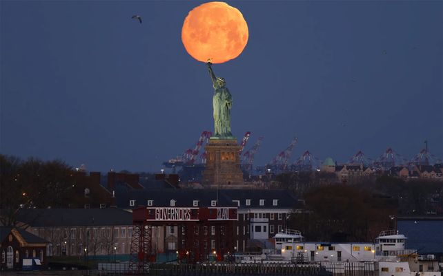 La superluna se pone detrás de la Estatua de la Libertad en la ciudad de Nueva York