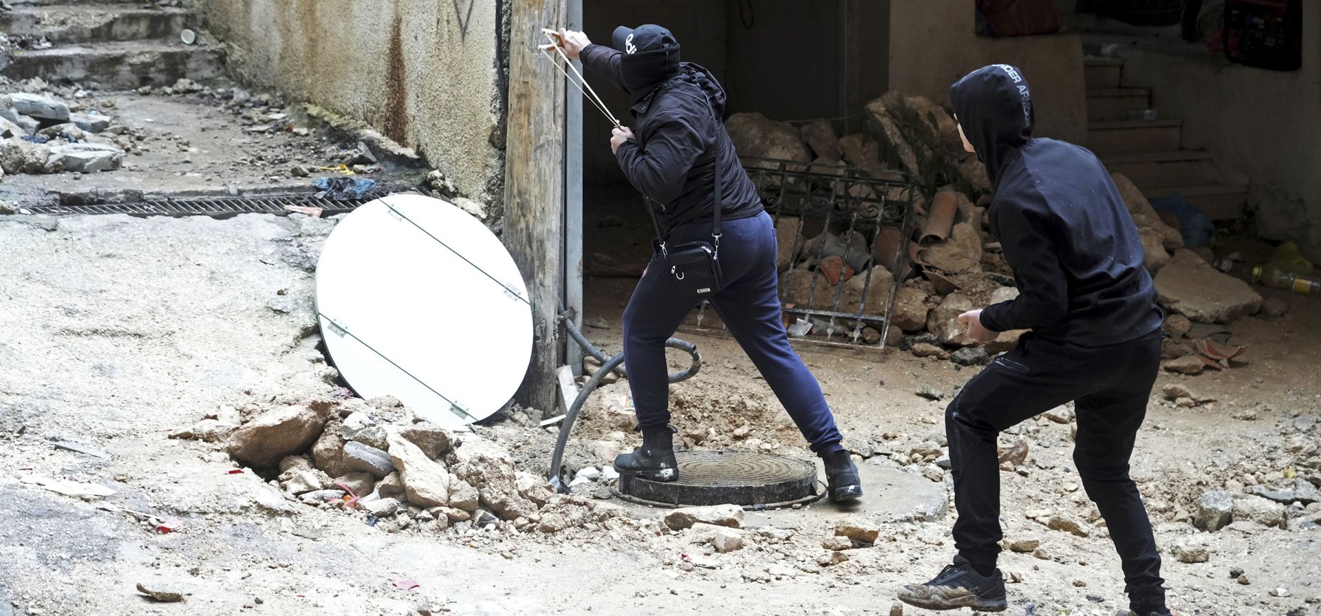 Palestinos usan hondas después de que las fuerzas de seguridad israelíes demolieran la casa de la familia del militante palestino Fadi Abu Shkhaidem, en el campo de refugiados de Shuafat en Jerusalén, el martes 1 de febrero de 2022.