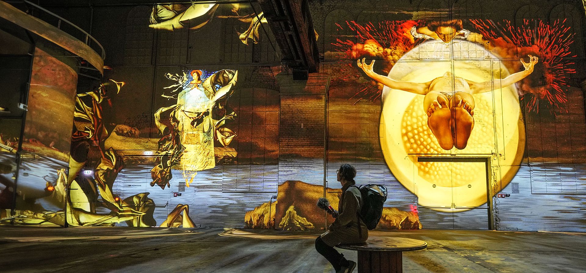 Visitantes ven obras de arte multimedia digitales proyectadas en las paredes de una antigua acería del artista surrealista español Salvador Dalí en el Phoenix des Lumieres, en Dortmund, Alemania, el jueves 25 de enero de 2024. (Foto AP /Martín Meissner)