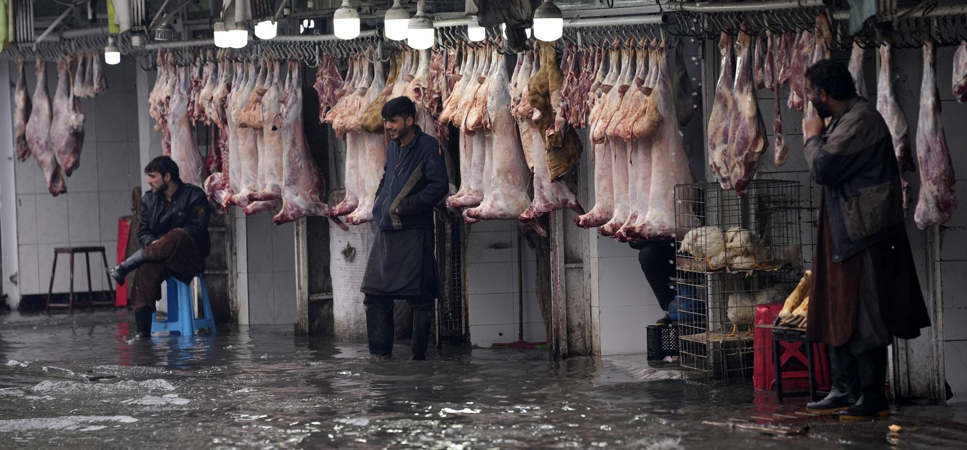 Carniceros afganos frente esperan clientes en sus tiendas, en una calle inundada durante un día lluvioso y nevado, en Kabul, Afganistán, el martes 22 de febrero de 2022.