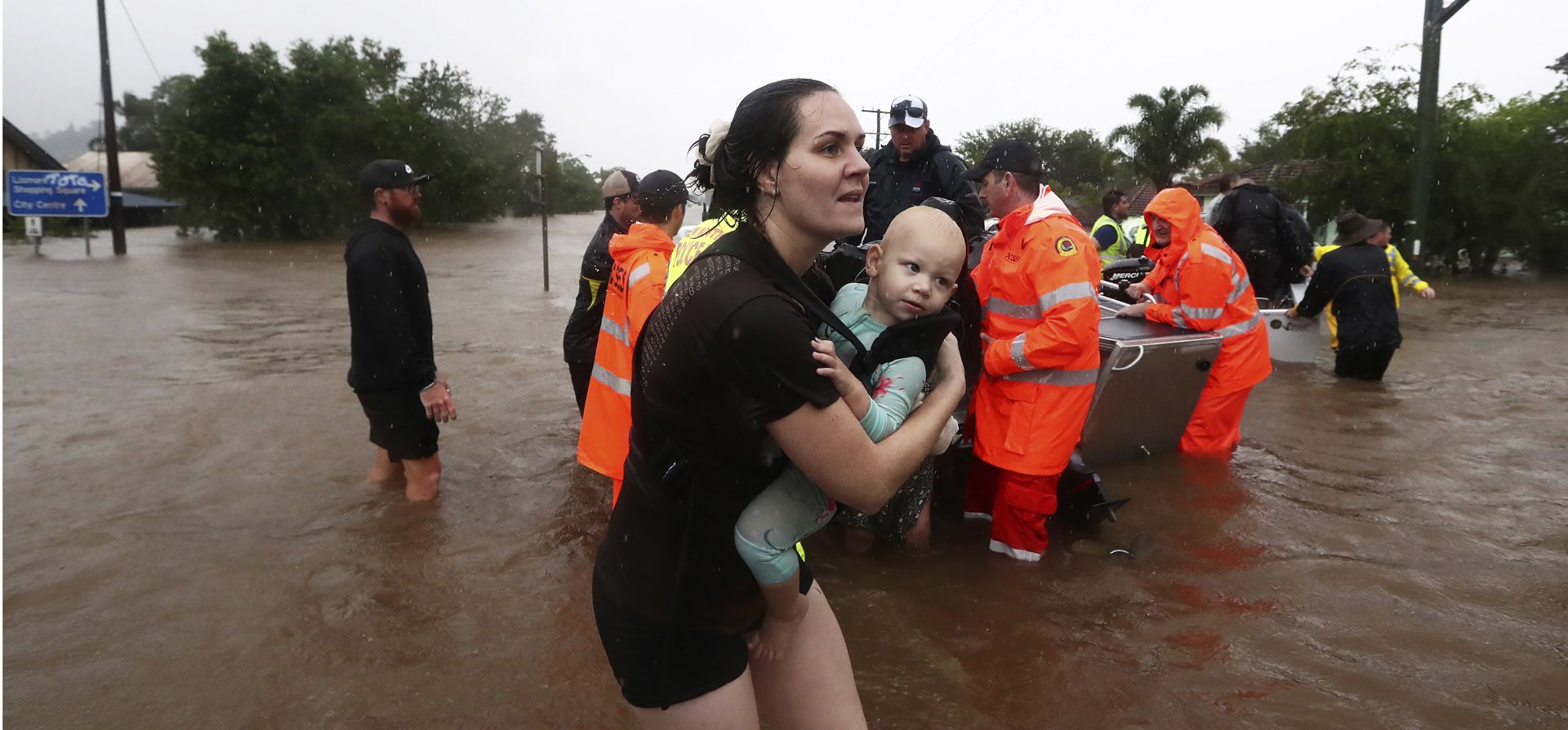 Una mujer carga a un bebé mientras la gente usa botes pequeños para trasladarse a través de las inundaciones en Lismore, Australia, el lunes 28 de febrero de 2022. Las fuertes lluvias están provocando inundaciones récord en algunas áreas de la costa este.