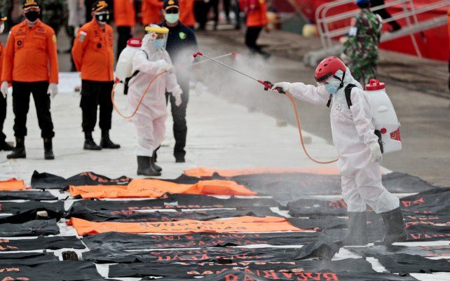 Miembros de la Cruz Roja Indonesia rocían desinfectante en bolsas para cadáveres que contienen restos humanos recuperados del mar de Java, donde el vuelo SJ-182 de Sriwijaya Air se estrelló el sábado, en el puerto de Tanjung Priok en Yakarta, Indonesia.