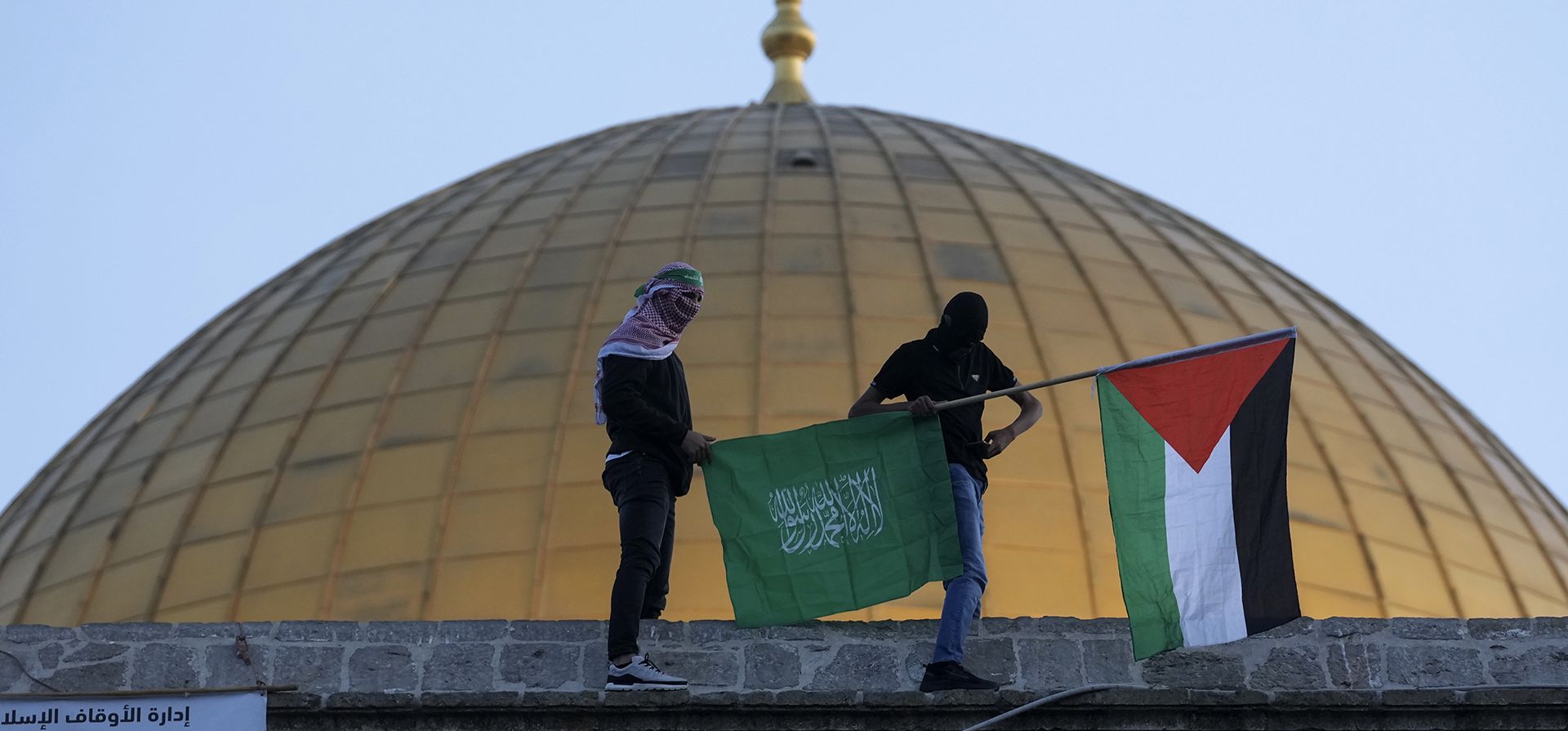 Palestinos enmascarados portan una bandera palestina durante las celebraciones de Eid al-Fitr junto a la Mezquita de la Cúpula de la Roca en el complejo de la Mezquita de Al-Aqsa en la Ciudad Vieja de Jerusalén, el lunes 2 de mayo de 2022.