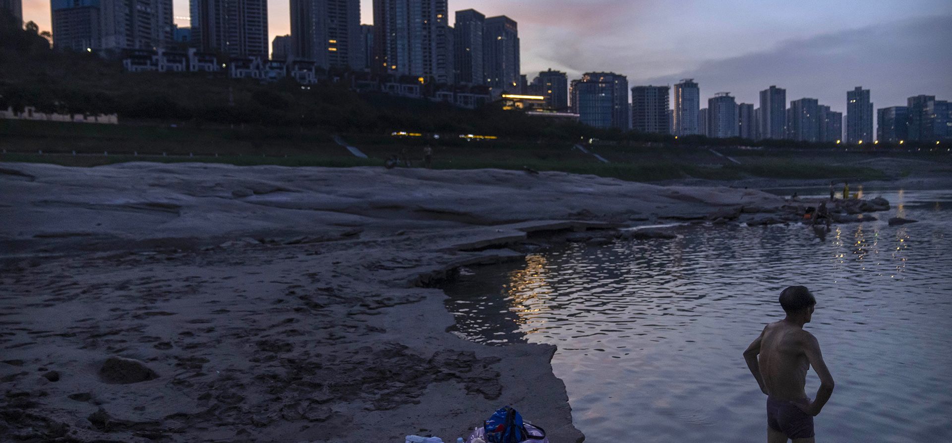 Un hombre se encuentra en aguas poco profundas cerca del lecho seco del río Yangtze en la municipalidad de Chongqing, en el suroeste de China, el viernes 19 de agosto de 2022. Los barcos se deslizan por el medio del Yangtze, después de que el verano más seco en seis décadas dejó uno de los ríos más poderoso a la mitad de su ancho normal.