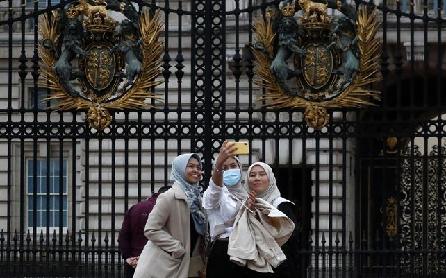 Turistas posan para selfies frente a las puertas del Palacio de Buckingham en Londres. El gobierno británico dice que todas las personas asintomáticas en Inglaterra podrán hacerse dos pruebas gratuitas de coronavirus por semana