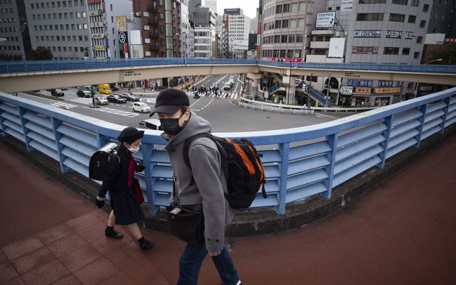 Un hombre y un estudiante de primaria caminan uno al lado del otro en un paso elevado para peatones en Tokio. Las autoridades destacan la buena acogida de sus medidas contra el coronavirus.