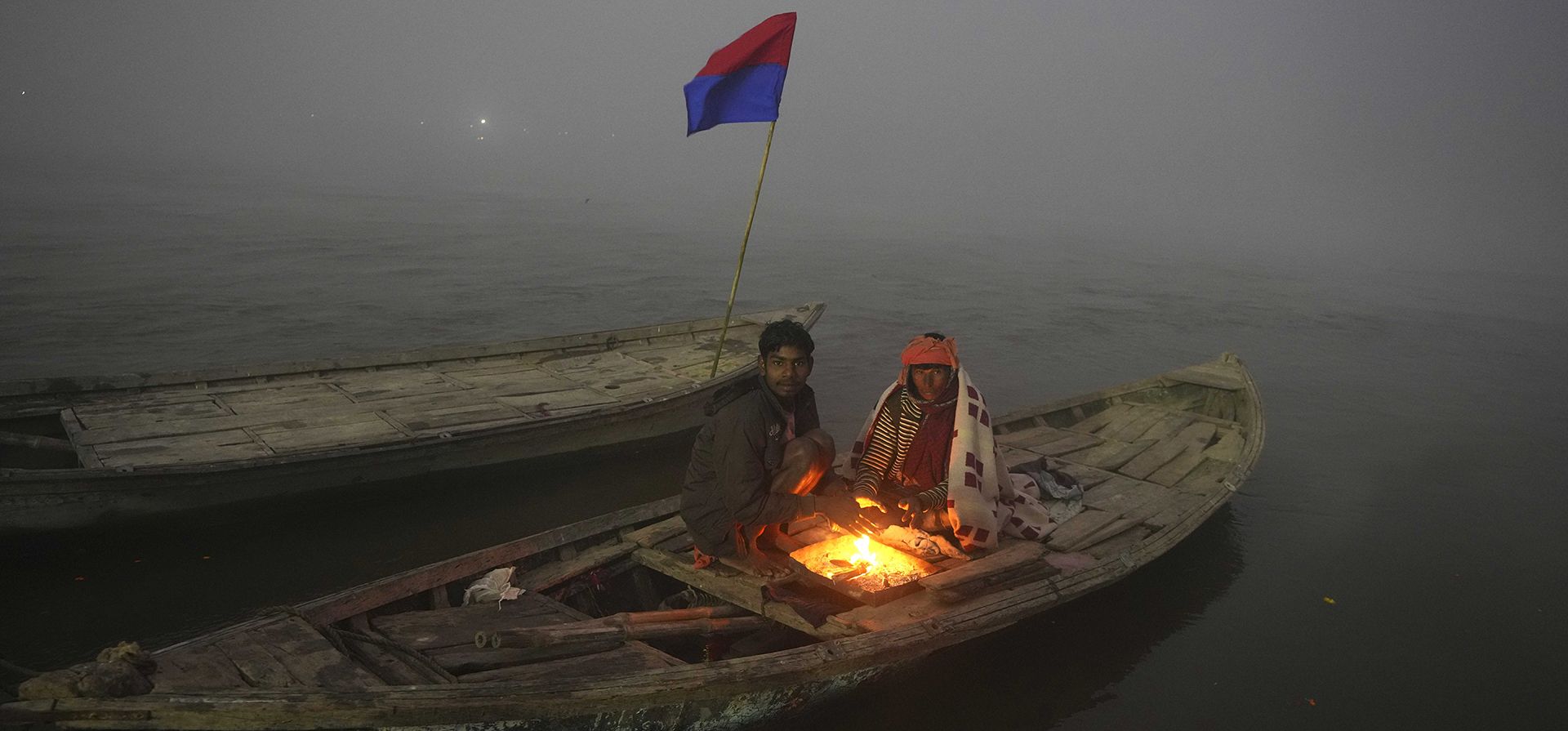 Los tripulantes de un bote se mantienen calientes alrededor de una fogata en el punto de encuentro de los ríos Ganges y Yamuna, el día de Paush Purnima durante la feria tradicional anual Magh Mela en Prayagraj, en el estado norteño indio de Uttar Pradesh, el viernes 6 de enero de 2023. (Foto AP/Rajesh Kumar Singh)