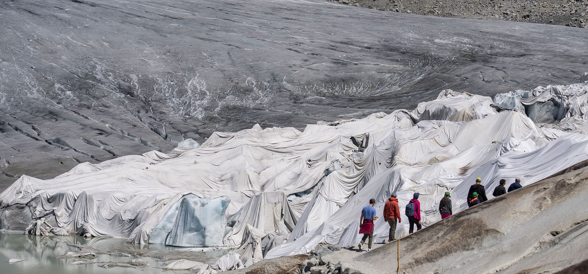 La gente visita el glaciar del Ródano cubierta con mantas sobre Gletsch cerca de Furkapass en Suiza, el miércoles 13 de julio de 2022. El glaciar más antiguo de los Alpes está protegido por mantas blancas especiales para evitar que se derrita.