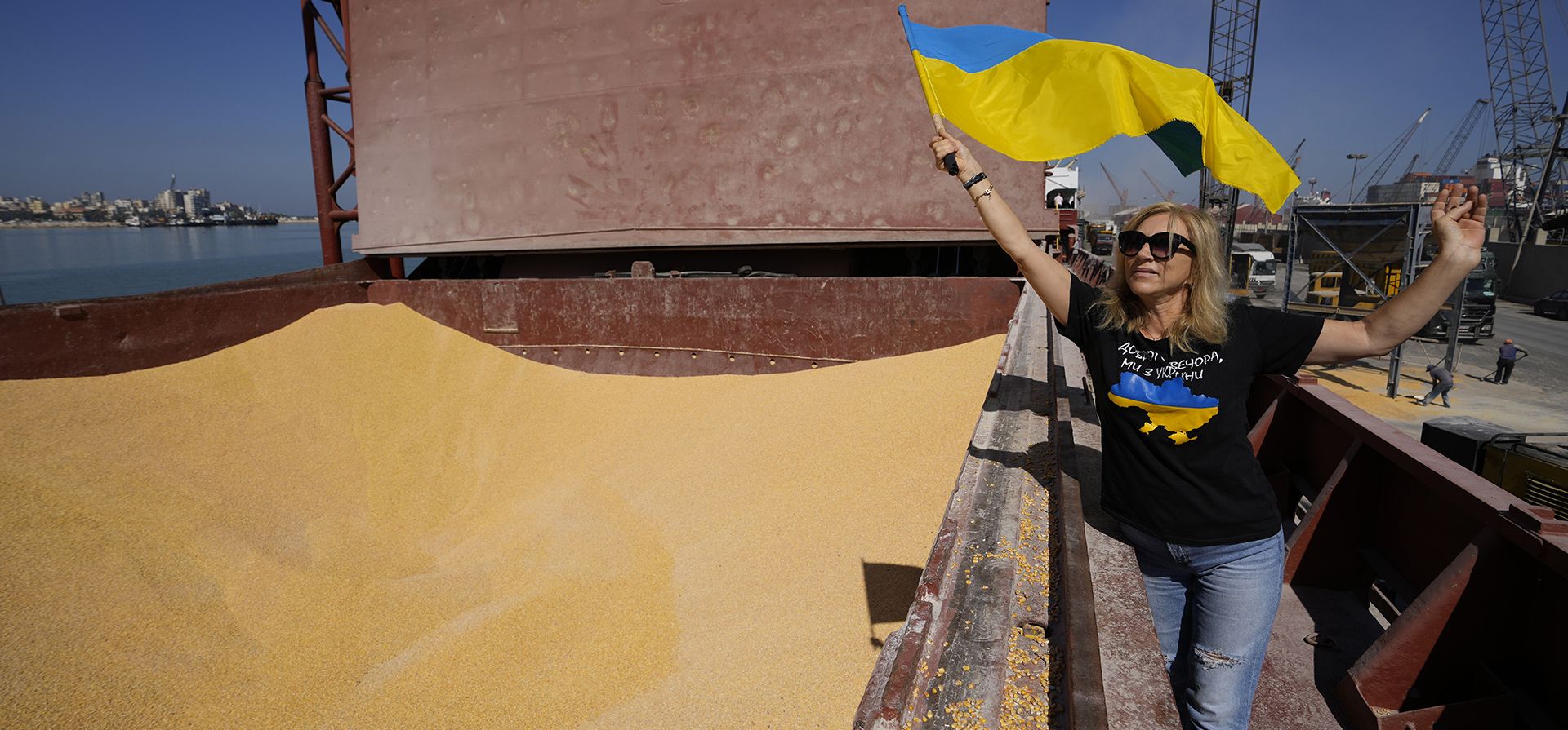 Una mujer ucraniana que vive en el Líbano ondea la bandera nacional ucraniana mientras los camiones se llenan con maíz ucraniano del barco AK Ambition, que navega bajo la bandera de Panamá en el puerto marítimo de Trípoli, en el norte del Líbano, el lunes 26 de septiembre de 2022.