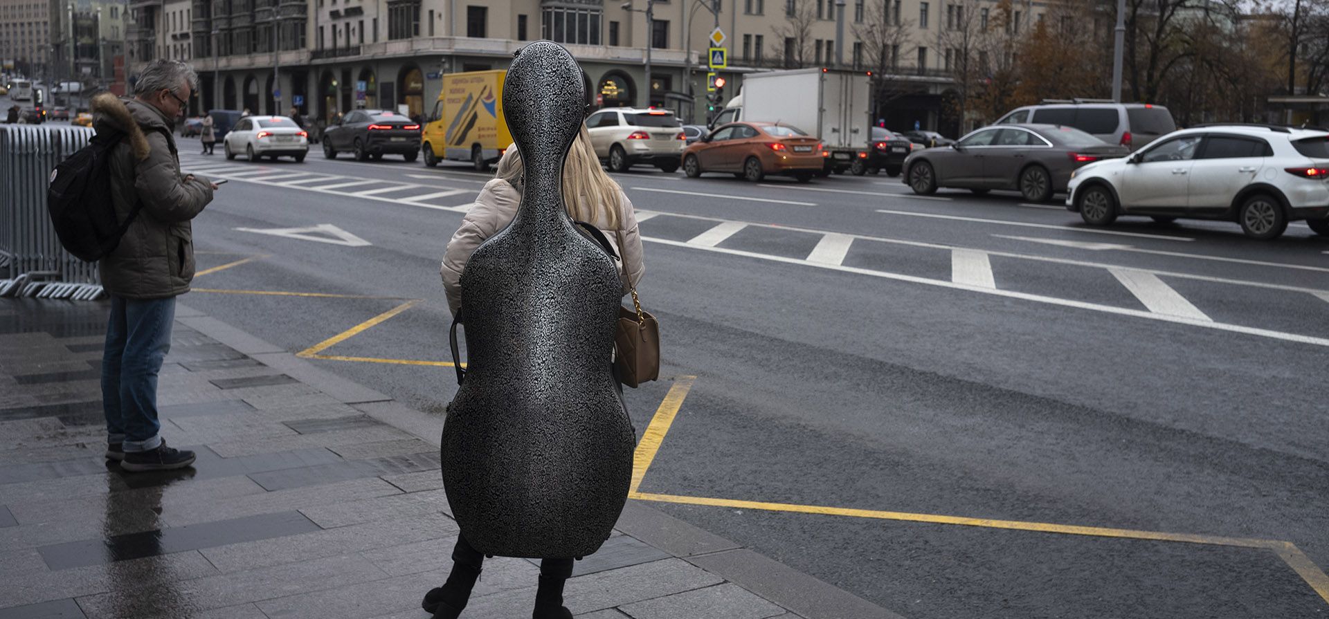 Una mujer con un violonchelo en una parada de autobús cerca del Teatro Bolshoi y el histórico Hotel Metropol al fondo en Moscú, Rusia, el miércoles 9 de noviembre de 2022.