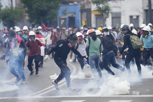 Un manifestante corre para atrapar un bote de gas lacrimógeno lanzado por la policía, otros huyen del lugar corriendo. 