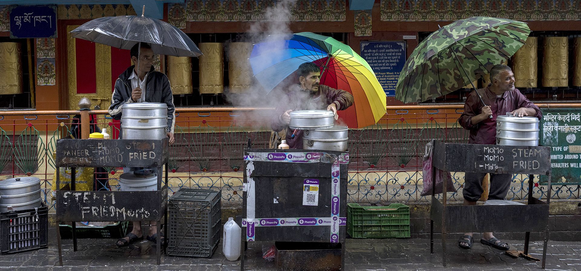 Los vendedores que venden albóndigas tibetanas cortejan a los clientes mientras se protegen de la lluvia en Dharmsala, India, el jueves 30 de junio de 2022.