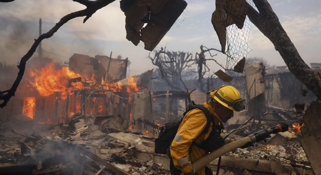 Un bombero combate un incendio alrededor de una estructura calcinada en el vecindario de Pacific Palisades.