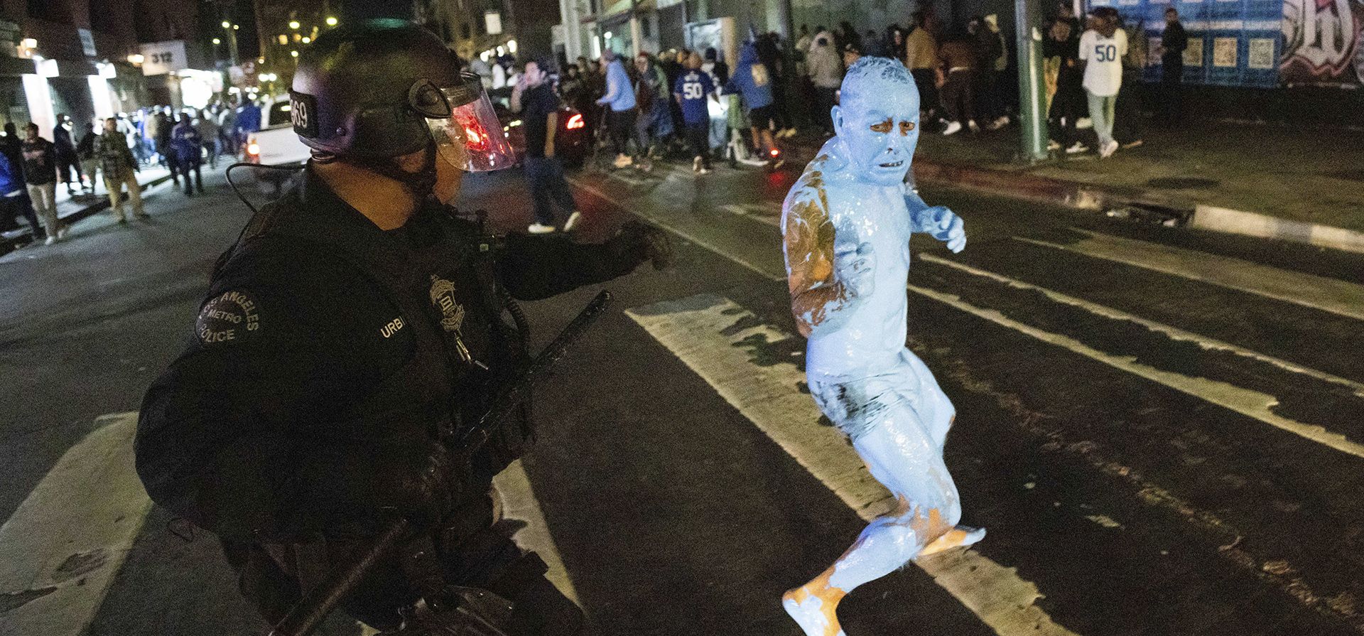 Una persona cubierta de pintura azul huye de un policía mientras los aficionados celebran en las calles después de que los Dodgers de Los Ángeles ganaron contra los Yankees de Nueva York en la Serie Mundial de béisbol el miércoles 30 de octubre de 2024 en Los Ángeles. (Foto AP/Ethan Swope)