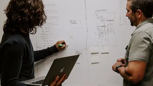 Two men stand by a whiteboard, collaborating on ideas related to an enterprise search platform