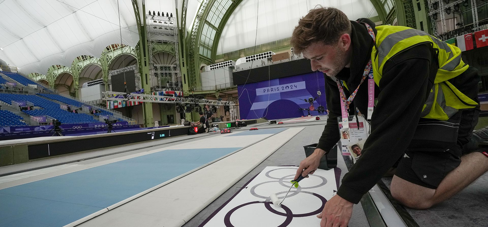 Un operario pinta los anillos olímpicos junto a una pista de esgrima mientras los trabajadores dan los toques finales al Gran Palais, el lugar que albergará la esgrima y el taekwondo en los Juegos Olímpicos de verano de 2024, el martes 23 de julio de 2024, en París, Francia. (Foto AP/Andrew Medichini) Un operario pinta los anillos olímpicos junto a una pista de esgrima mientras los trabajadores dan los toques finales al Gran Palais, el lugar que albergará la esgrima y el taekwondo en los Juegos Olímpicos de verano de 2024, el martes 23 de julio de 2024, en París, Francia. (Foto AP/Andrew Medichini)