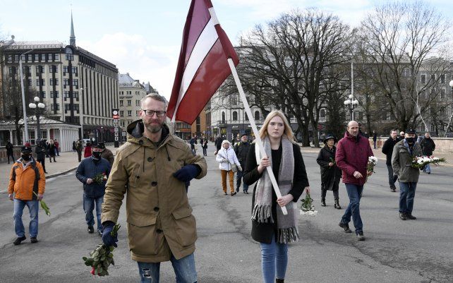 Una mujer camina con una bandera nacional de Letonia, para depositar flores en el Monumento a la Libertad en la conmemoración a los soldados que lucharon en una unidad de las Waffen SS nazis durante la Segunda Guerra Mundial, en Riga, Letonia.
