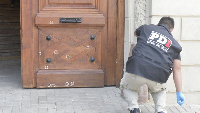 las huellas del ataque. Un policía del gabinete criminalístico identifica los orificios que los balazos dejaron en la puerta del Concejo.