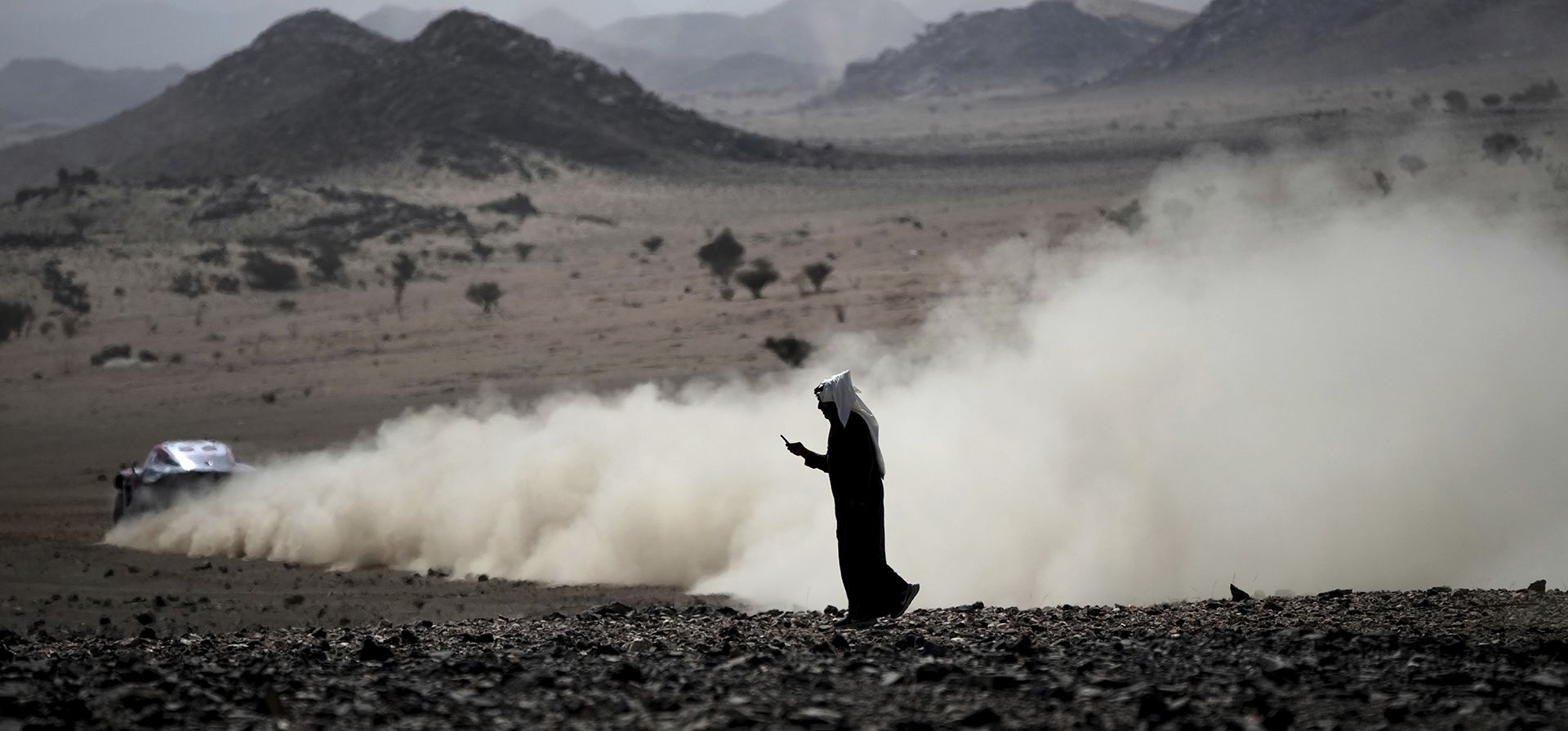 Un hombre mira su teléfono durante el prólogo del Rally Dakar en Bisha, Arabia Saudita, el viernes 3 de enero de 2025. (Foto AP/Christophe Ena)