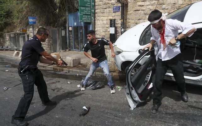 Un oficial de policía israelí apunta con una pistola a un hombre palestino