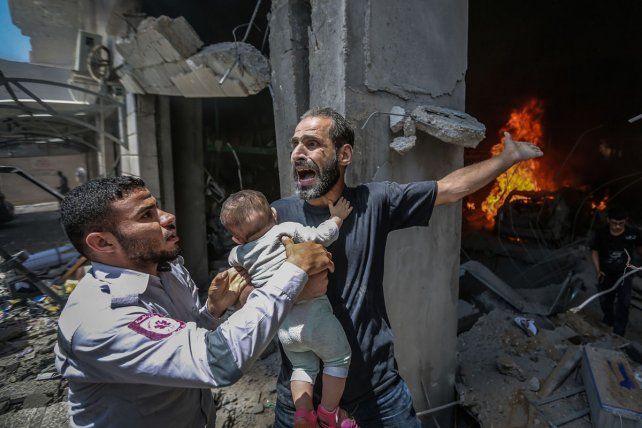 Un hombre palestino sostiene a su bebé y reacciona después de que su casa fuera alcanzada durante un ataque aéreo israelí, en medio del estallido de la violencia israelí-palestina, en la ciudad de Gaza.