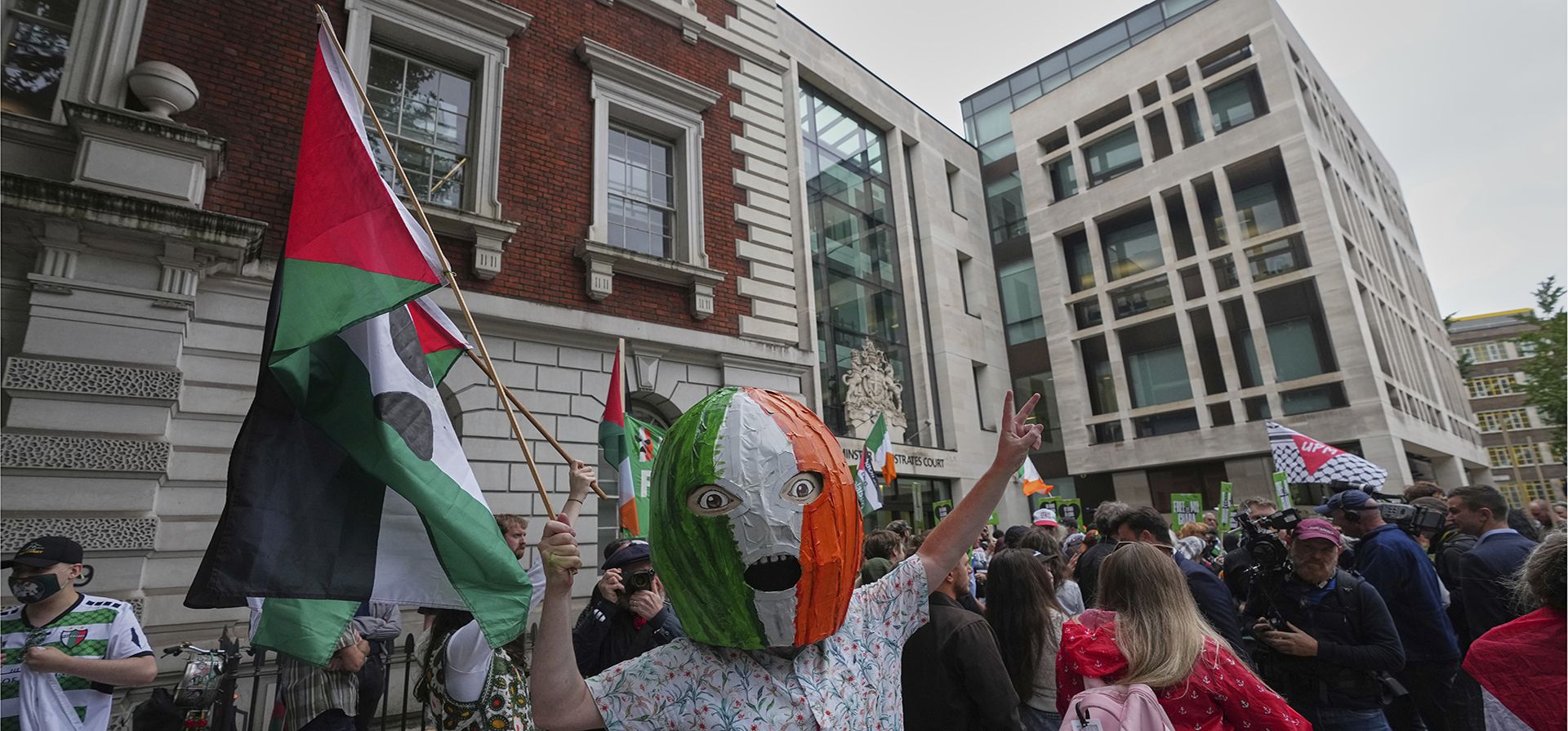 Simpatizantes de Liam Óg Ó hAnnaidh, también conocido como Mo Chara, miembro de la banda irlandesa Kneecap, esperan con pancartas y banderas su llegada al Tribunal de Magistrados de Westminster, Londres, el miércoles 20 de agosto de 2025, donde se le acusa de un delito de terrorismo por exhibir una bandera en apoyo a Hezbolá durante una actuación con la banda en noviembre de 2024. (Foto AP/Frank Augstein)
