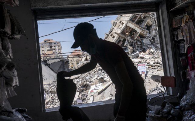 Un empleado de una pequeña empresa, limpia el polvo de concreto y los escombros de una tienda después de que un ataque aéreo destruyera un edificio vecino antes de un alto el fuego que detuvo una guerra de 11 días entre los gobernantes de Hamas de Gaza e Israel.