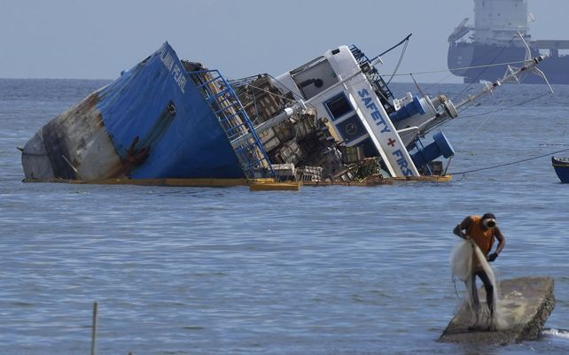 Un pescador fija su red al lado de un buque semi hundido después de que chocara con una draga con bandera de Chipre en la bahía de Manila