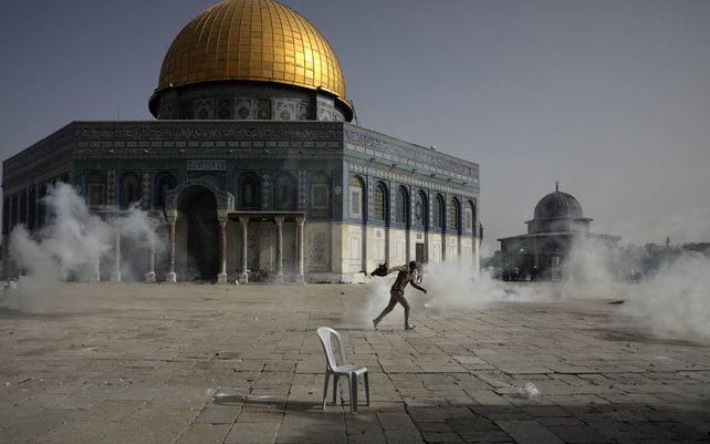 Un palestino huye de los gases lacrimógenos durante los enfrentamientos con las fuerzas de seguridad israelíes frente a la Mezquita de la Cúpula de la Roca en el recinto de la Mezquita Al Aqsa en la Ciudad Vieja de Jerusalén.