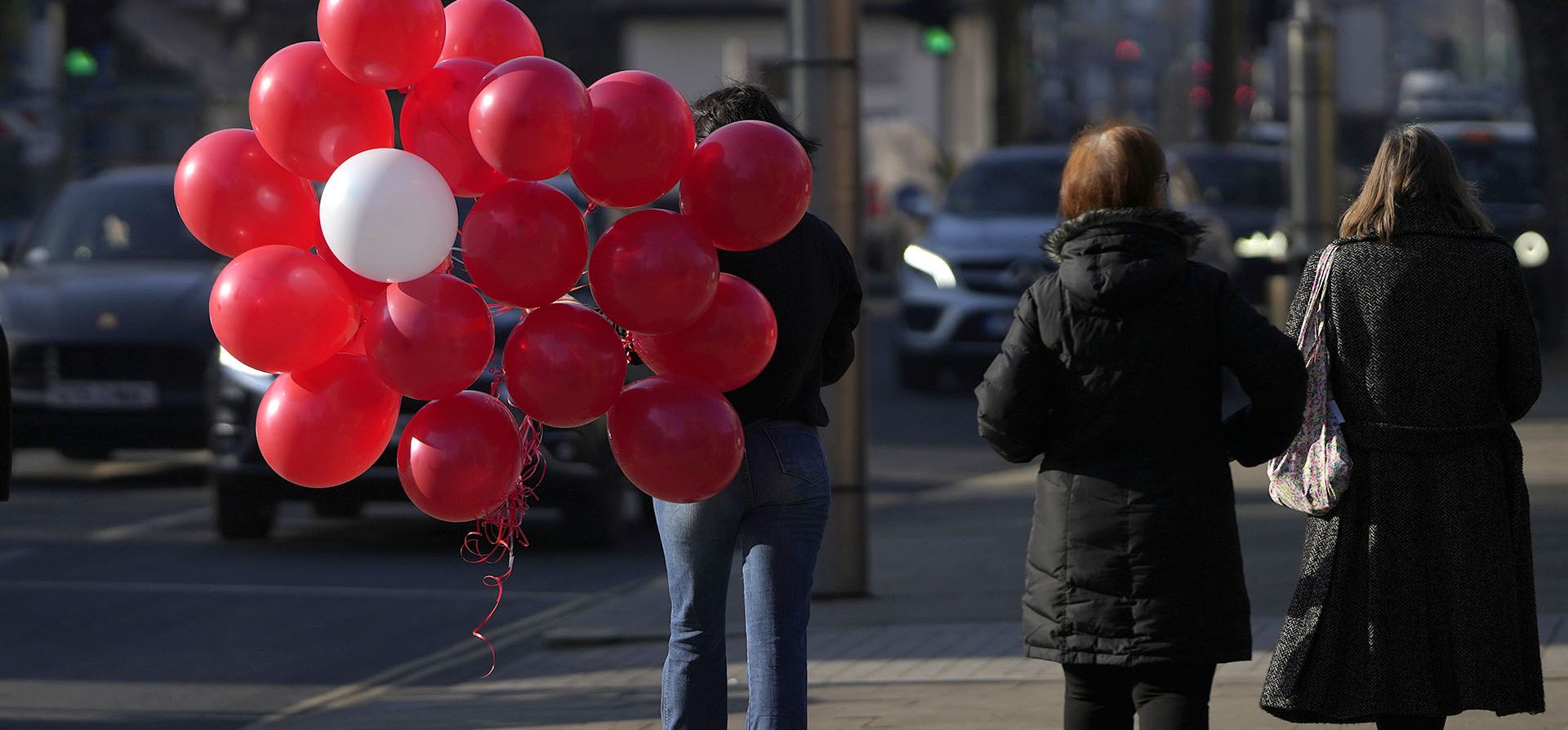 Una mujer sostiene una colección de globos rojos y uno blanco mientras camina hacia su automóvil el Día de San Valentín en Londres, el martes 14 de febrero de 2023. (Foto AP/Alastair Grant)