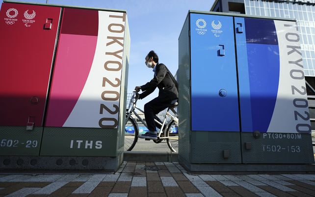 Un hombre pasa en bicicleta frente a algunos anuncios de los Juegos Olímpicos y Paralímpicos de Tokio 2020.