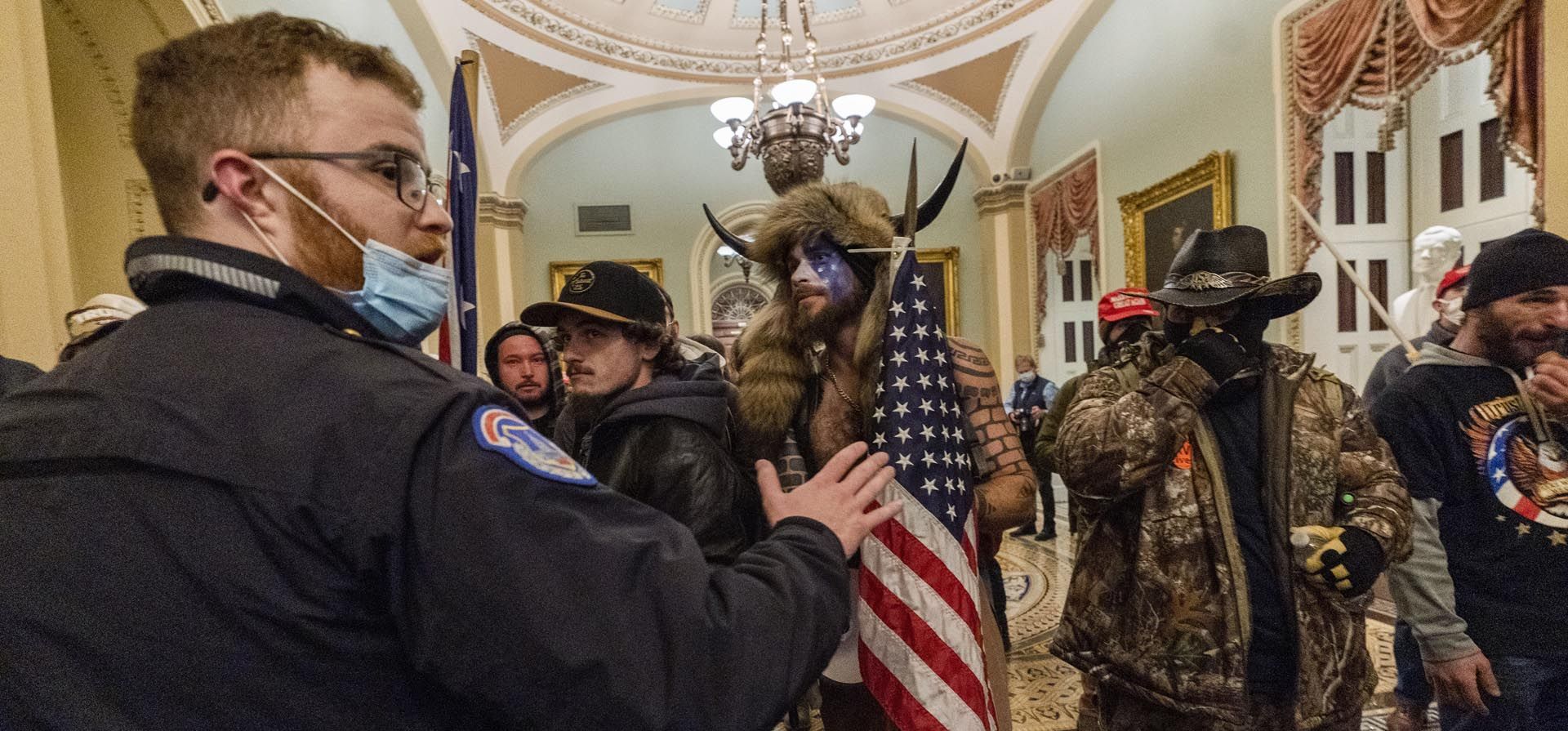 Jacob Anthony Chansley, con su icónico atuendo junto a otros insurrectos que apoyaban al entonces presidente Donald Trump, son confrontados por la Policía del Capitolio de los Estados Unidos en el pasillo fuera de la cámara del Senado en el Capitolio, el 6 de enero de 2021, en Washington.