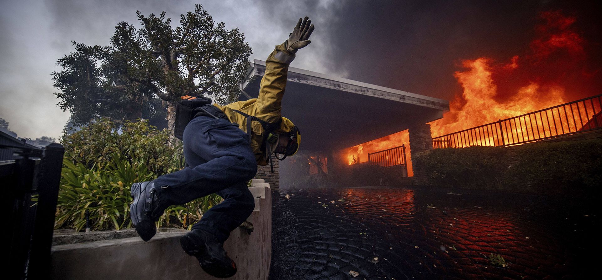 Un bombero salta una valla mientras combate el incendio de Palisades en el barrio de Pacific Palisades de Los Ángeles, el martes 7 de enero de 2025. (Foto AP/Ethan Swope)