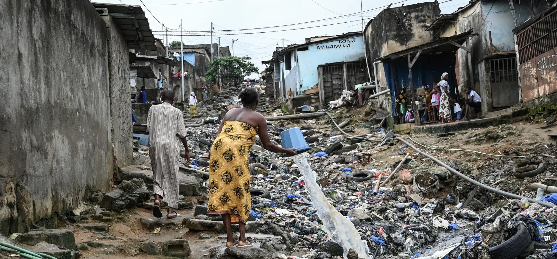 Una mujer vierte agua en una calle llena de residuos plásticos en una comuna de Abiyán, Attecoube, Costa de Marfil. Fotografía: Sia Kambou/AFP/Getty Images Una mujer vierte agua en una calle llena de residuos plásticos en una comuna de Abiyán, Attecoube, Costa de Marfil. Fotografía: Sia Kambou/AFP/Getty Images