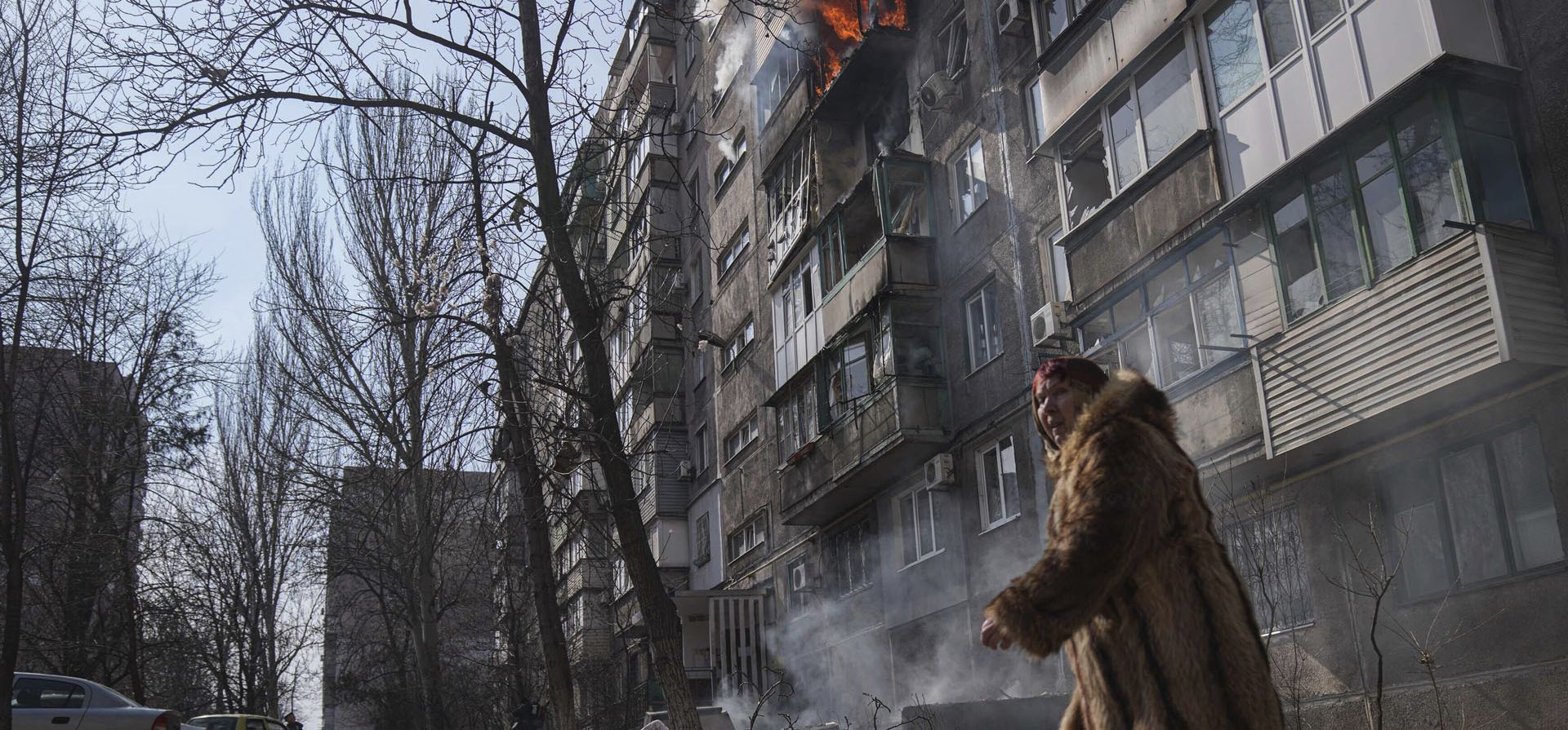 Una mujer pasa junto a un edificio de apartamentos en llamas después de que Rusia efectuara otro bombardeo en Mariupol, Ucrania.