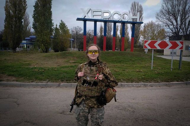 Una joven soldado ucraniana posa ante el cartel de ingreso a Jersón (en cirílico). La ciudad sufrió casi 9 meses de ocupación rusa.&nbsp;