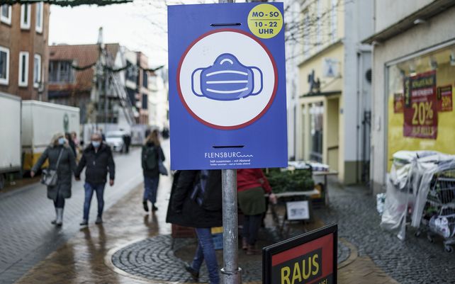 Un letrero que indica las restricciones COVID-19 de máscaras obligatorias cuelga de un poste a lo largo de una calle peatonal en Flensburg