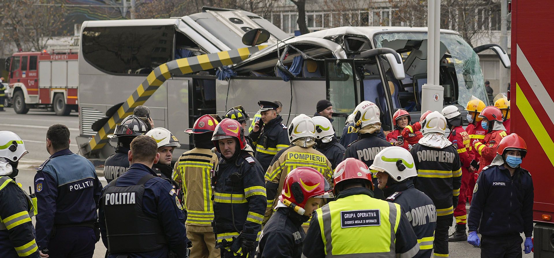Empleados del servicio de emergencia se paran alrededor de un autobús que transportaba a 47 ciudadanos griegos que se estrelló contra una barra de límite de altura en la entrada de un túnel en Bucarest, Rumania, el viernes 23 de diciembre de 2022. El jefe del Departamento de Situaciones de Emergencia de Rumania (DSU) Raed Arafat dijo a los periodistas que 22 personas fueron hospitalizadas, una persona murió y otra se encuentra en estado crítico. (Foto AP/Vadim Ghirda)