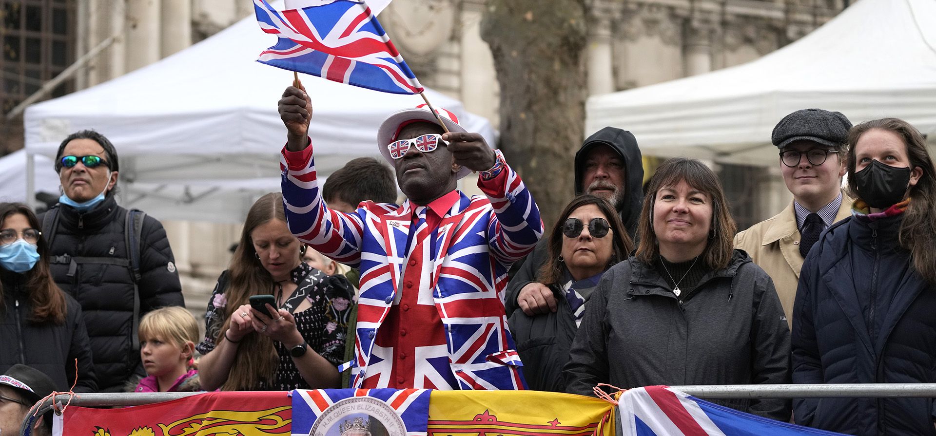 Un fanático real ondea una bandera que muestra a la reina Isabel II mientras la multitud se reúne antes de un servicio de acción de gracias por la vida del príncipe Felipe, duque de Edimburgo en la Abadía de Westminster en Londres, el martes 29 de marzo de 2022.