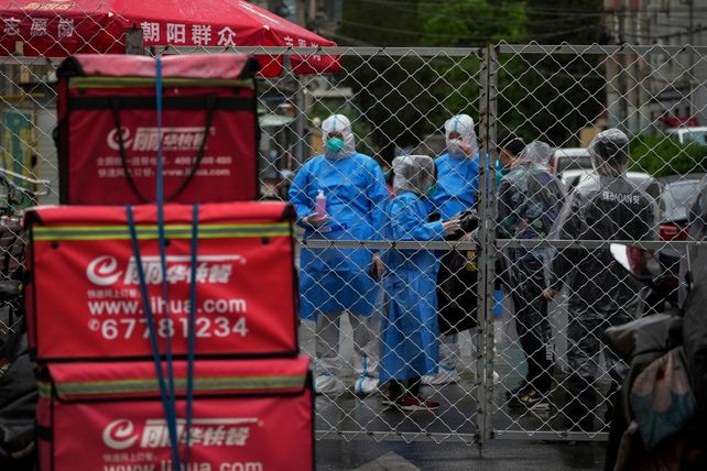 Agentes sanitarios de Shanghái lucen apostados detrás de la alambrada que separa a un barrio de la ciudad.&nbsp;