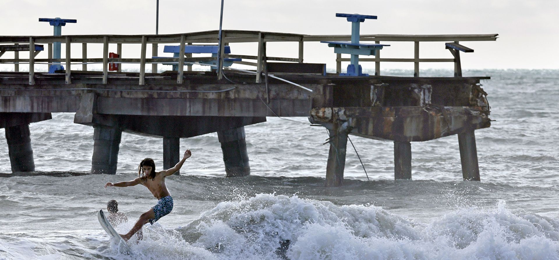 Los surfistas surcan las olas en la playa de Lauderdale-by-the-Sea frente a una sección del muelle de pesca de Anglin que se derrumbó debido a la tormenta tropical Nicole, el jueves 10 de noviembre de 2022.